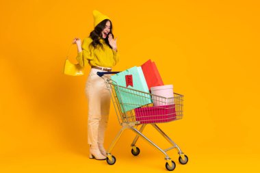 White woman making fun while posing with shopping cart isolated over yellow background
