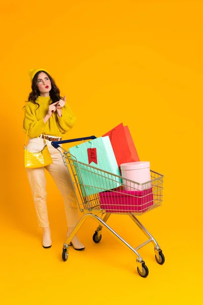 White Puzzled Woman Gesturing While Posing Shopping Cart Isolated Yellow — Foto de Stock