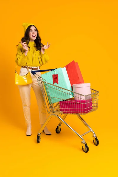 White Excited Woman Gesturing While Posing Shopping Cart Isolated Yellow — Photo