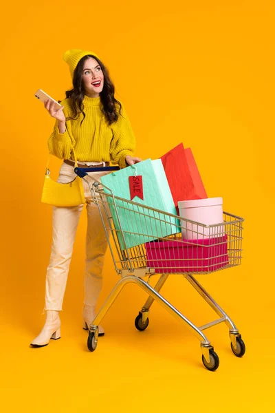 White Excited Woman Posing Cellphone Shopping Cart Isolated Yellow Background — Foto de Stock