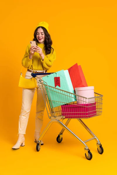 White Excited Woman Posing Cellphone Shopping Cart Isolated Yellow Background — Photo
