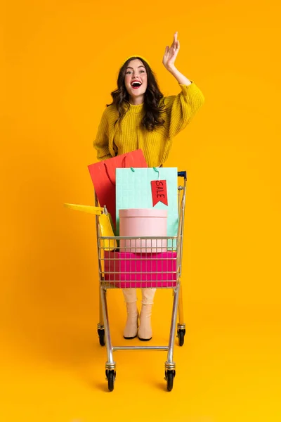 White Excited Woman Gesturing While Posing Shopping Cart Isolated Yellow — Photo