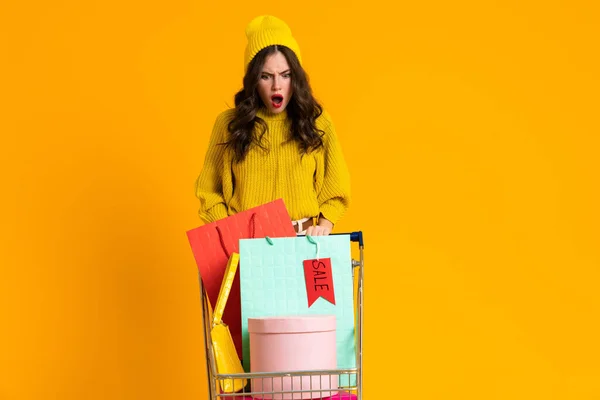 Displeased Woman Expressing Surprise While Posing Shopping Cart Isolated Yellow — Foto de Stock