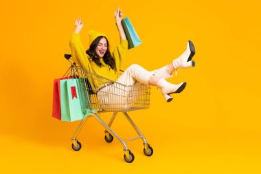 White excited woman making fun in shopping cart isolated over yellow background