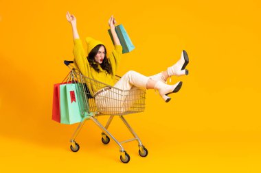 White excited woman making fun in shopping cart isolated over yellow background