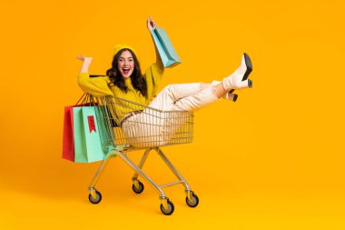 White excited woman making fun in shopping cart isolated over yellow background