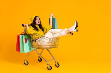 White excited woman making fun in shopping cart isolated over yellow background