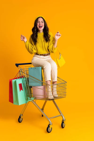 Sarı Arka Planda Izole Edilmiş Alışveriş Arabasında Oturan Beyaz Kadın — Stok fotoğraf