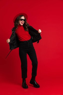White woman in leather jacket laughing while dancing on camera isolated over red background