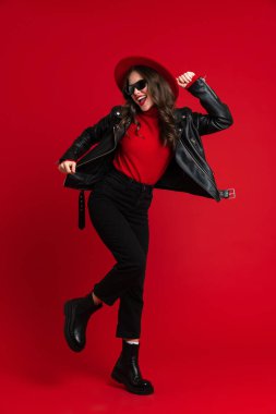 White woman in leather jacket laughing while dancing on camera isolated over red background