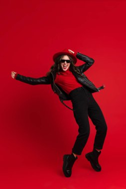 White woman in leather jacket laughing while dancing on camera isolated over red background