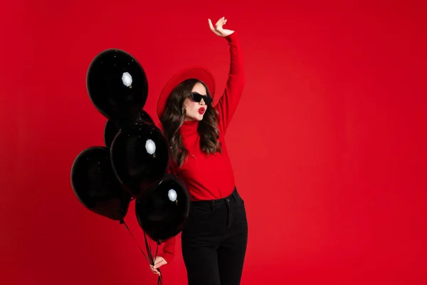 Kırmızı Arka Planda Siyah Balonlarla Poz Veren Şapkalı Beyaz Kadın — Stok fotoğraf
