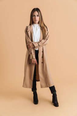 Beyaz bir kadın ceketini giyiyor ve bej arka planda izole edilmiş kameraya bakıyor.