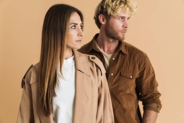 Beyaz sarışın çift bej arka planda yalnız poz verirken yana bakıyor.