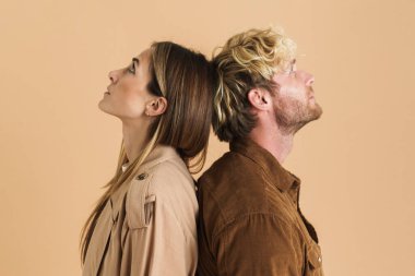 Beyaz çift zıt yönlere bakarken bej arka planda izole bir şekilde sırt sırta poz veriyor.