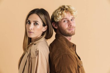 Beyaz çift bej arka planda izole bir şekilde sırt sırta poz verirken kameraya bakıyor