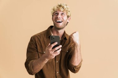 Beyaz sarışın adam, bej arka planda izole edilmiş bir cep telefonu kullanarak birinci sınıf jest yapıyor.