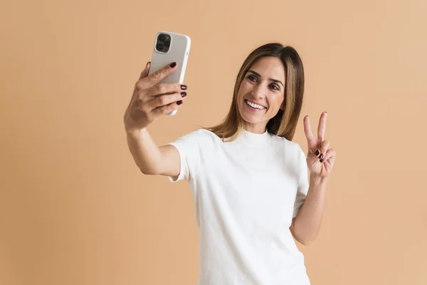 White Mid Woman Gesturing While Taking Selfie Cellphone Isolated Beige — стоковое фото