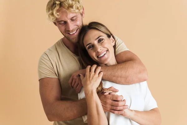 White couple wearing t-shirts hugging and laughing together isolated over beige background