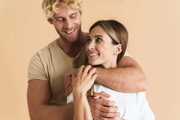 White couple wearing t-shirts hugging and laughing together isolated over beige background