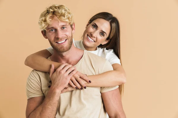 White couple wearing t-shirts hugging and smiling at camera isolated over beige background