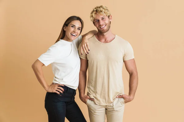 White couple wearing t-shirts posing and smiling at camera isolated over beige background