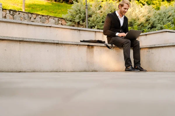 Blonde Man Working Laptop While Sitting Stone Bench Outdoors — Foto Stock