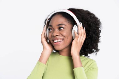 Beyaz arka planda izole edilmiş kulaklıklarla müzik dinlerken gülümseyen genç siyah kadın.