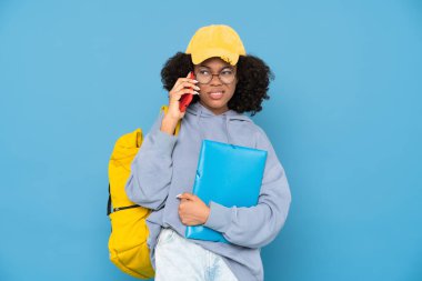 Mavi arka planda izole edilmiş klasörle poz verirken cep telefonuyla konuşan siyah bir kadın.