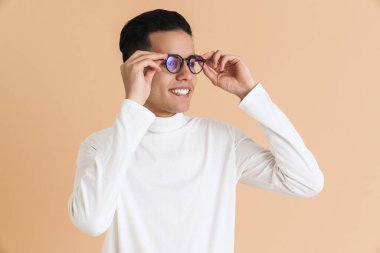 Genç, orta doğulu bir adam gülümsüyor ve bej arka planda soyutlanmış bir şekilde yan tarafa bakıyor.