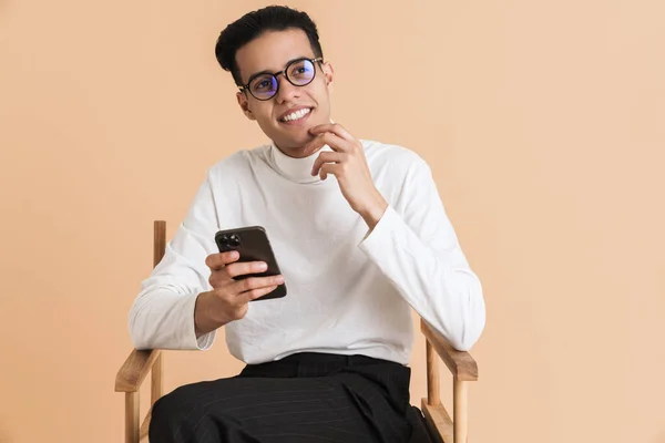 Young Middle Eastern Man Using Cellphone While Sitting Chair Isolated — Stockfoto