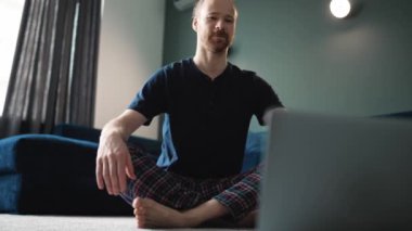 Handsome blond man wearing blue t-shirt doing yoga meditation on the floor at home