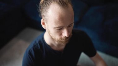 Mavi tişört giyen kendine güvenen sarışın adam evde yerde yoga meditasyonu yapıyor.