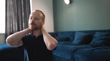 Mavi tişört giyen güzel sarışın adam evde boynunu yoğuruyor.