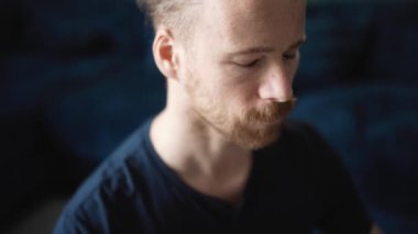 Mavi tişört giyen konsantre sarışın adam evde yoga meditasyonu yapıyor.
