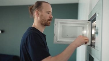 Concentrated blond man heats food in the microwave at home