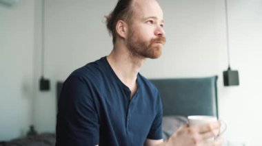 Dalgın sarışın adam kahve içiyor ve evde otururken manzaraya bakıyor.