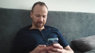 Güzel sarışın adam evde yatakta otururken akıllı telefondan mesaj atıyor.