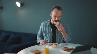 Yoğunlaşmış sarışın adam ekmek yiyor ve sabah evde etrafına bakıyor.