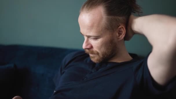 Concentrated Blond Man Wearing Pajama Typing Phone While Sitting Sofa — Vídeo de stock