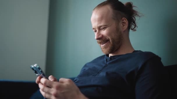 Positive Blond Man Wearing Pajama Typing Mobile While Sitting Sofa — Stock Video