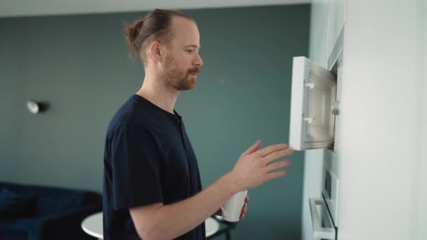 Concentrated Blond Man Heats Cup Water Microwave Home — Stock Video