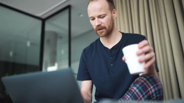 Confident Blond Man Holding Cup Looking Laptop While Sitting Home — Stockvideo