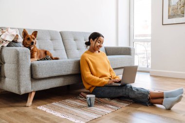 Evde dizüstü bilgisayarla çalışırken çay içen genç İspanyol kadın.
