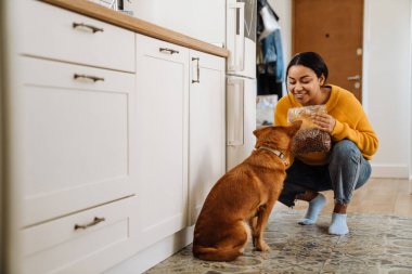 Genç İspanyol kadın mutfakta köpeğini beslerken gülümsüyor.