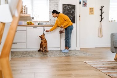 Genç İspanyol kadın mutfakta köpeğini beslerken gülümsüyor.