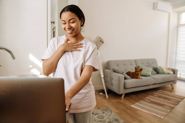 Young hispanic woman smiling and gesturing while using laptop at home