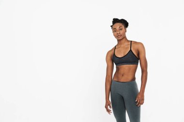 Genç siyah sporcu kadın beyaz arka planda yalnız poz veriyor ve kameraya bakıyor.