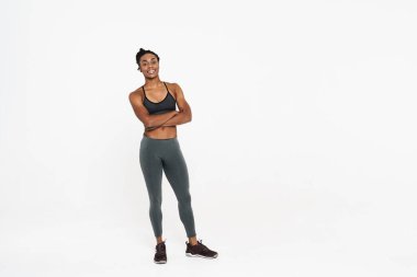 Genç siyah sporcu kadın gülümsüyor ve beyaz arka planda izole edilmiş kameraya bakıyor.