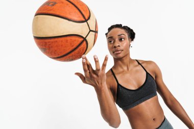 Black young sportswoman in earphones working out with basketball isolated over white background